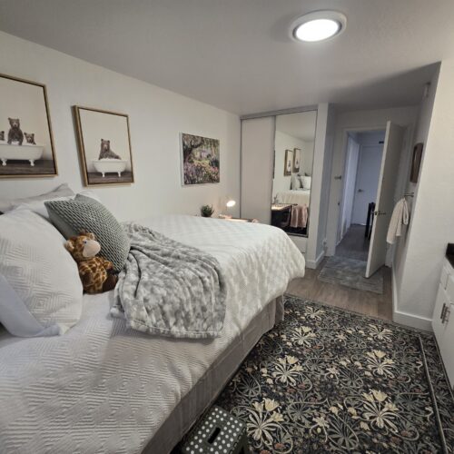 Cozy bedroom with two neatly made beds, grey and white bedding, a stuffed monkey, and bear-themed framed photos on the wall behind the beds.
