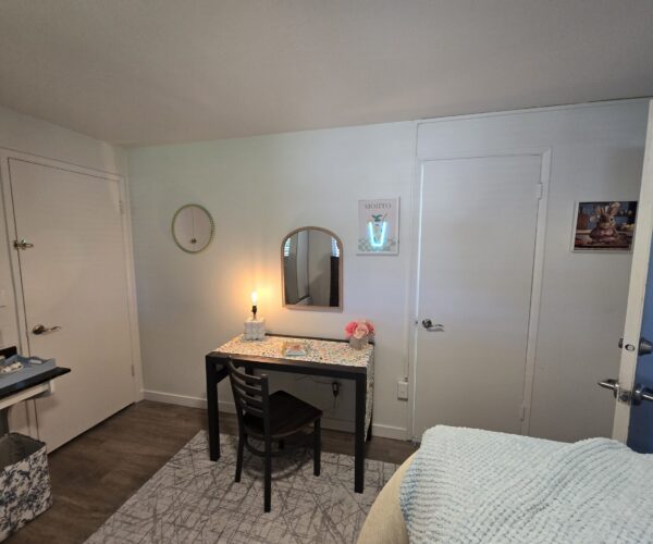 Corner of a bedroom with a black desk and two chairs, round wall mirror, and lit table lamp; pastel decor and mojito sign on wall.